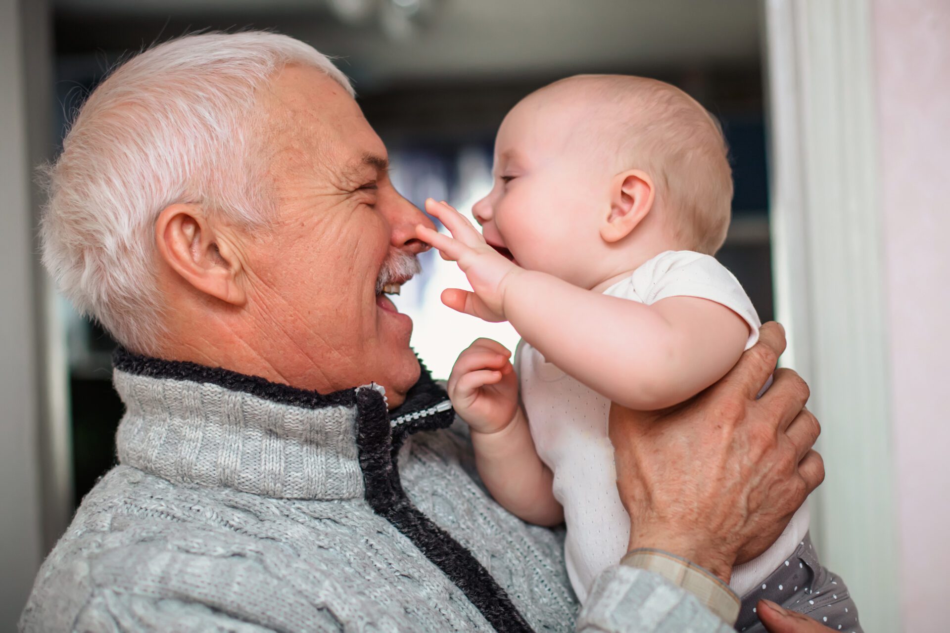 A newborn baby touches the old grandfather by the nose